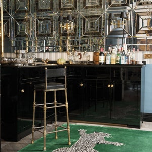 Pu&ograve; includere: Un'area bar lussuosa con una parete a specchio, mobili neri e un tappeto verde con un motivo leopardato. Uno sgabello da bar dorato con seduta nera &egrave; posizionato di fronte al bar. Bottiglie di liquore sono esposte sul bancone.
