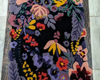 May include: A floral rug with a black background and a colorful array of flowers in shades of red, yellow, purple, and pink. The rug has a unique, irregular shape, and the flowers are densely packed.