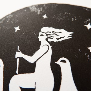 Peut inclure: Gravure sur linol&eacute;um en noir et blanc d'une femme &agrave; cheval avec un oiseau &agrave; ses c&ocirc;t&eacute;s, sur fond de ciel &eacute;toil&eacute;.