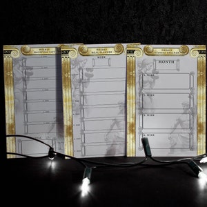 May include: Three white printable planners with gold accents. The planners are labelled "Weekly Shopping List", "Weekly Meal Planner", and "Weekly Fitness Tracker".