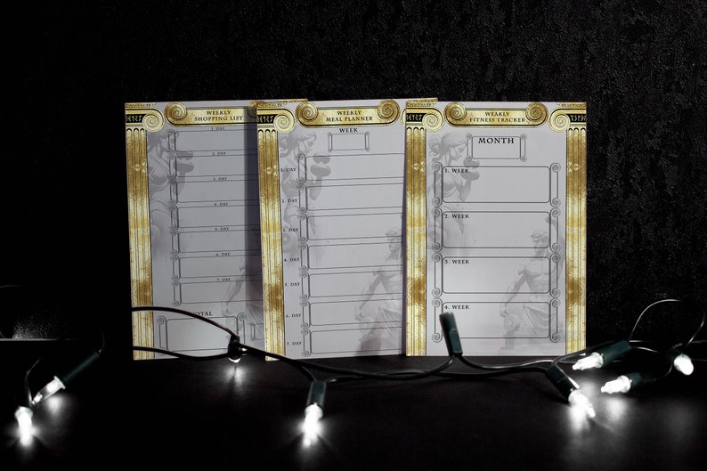 May include: Three white printable planners with gold accents. The planners are labelled "Weekly Shopping List", "Weekly Meal Planner", and "Weekly Fitness Tracker".