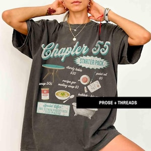 May include: A gray t-shirt with a vintage-style graphic that says "Chapter 55 Starter Pack". The graphic includes illustrations of a table, soup, a paint set, a bathtub, and a recipe for soup. The text "PROSE + THREADS" is printed in white at the bottom of the shirt.