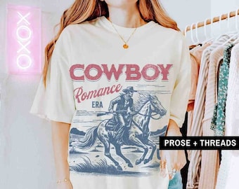 Peut inclure: Un t-shirt blanc avec un graphique vintage d'un cowboy à cheval. Le graphique comprend le texte "Cowboy Romance Era".