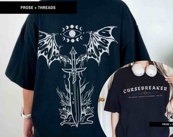 May include: Two black t-shirts with white graphic designs. The first shirt features a sword with wings and a crescent moon and eye design. The second shirt has the text "Cursebreaker" with the words "Spell Breaker, Defender of the Kingdom, High Lord" underneath.