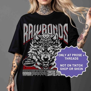 Op de afbeelding: Zwart T-shirt met een gedetailleerde wit en grijze wolf grafische afbeelding en de tekst "RAWRONDS". Extra tekst bevat "LIVE! FROM THE BONDED CITY" en "ONLY AT PROSE + THREADS".