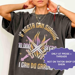 May include: Dark gray t-shirt with the text "IF NESTA CAN SURVIVE 10,000 STEPS I CAN DO GARDEN" in a gradient font. The design includes crossed swords and flames. The shirt also has the text "ONLY AT PROSE + THREADS NOT ON TIKTOK SHOP OR SHEIN".
