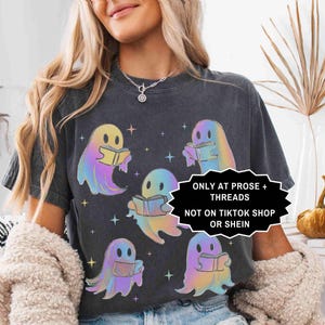 May include: Dark gray t-shirt featuring a design of six colorful ghost characters reading books. The ghosts have a rainbow gradient effect. The shirt also has the text "ONLY AT PROSE + THREADS NOT ON TIKTOK SHOP OR SHEIN".