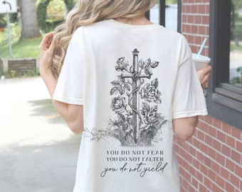 Może przedstawiać: Biały t-shirt z czarno-białym nadrukiem przedstawiającym miecz z różami i tekstem "You do not fear, You do not falter, You do not yield."