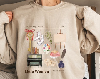 Könnte beinhalten: Beigefarbener Pullover mit einem grafischen Druck einer Schlüssel, Schlittschuhen, Büchern, einer Farbpalette, einem Pinsel, einer Stoffrolle, einem kleinen Staffelei, einem Klavier und Briefumschlägen. Der Text "Louisa May Alcott 1868 Little Women Meg, Jo, Beth and Amy" ist auf dem Pullover gedruckt.