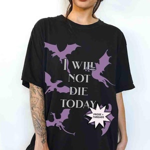 May include: Black oversized t-shirt with a purple graphic of dragons and the text "I will not die today". The shirt has a small purple tag with the text "Prose + Threads".