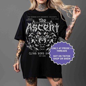 May include: Black t-shirt featuring a detailed wolf graphic with the text "The Ascent" and event details. The shirt also includes the text "Climb Bond Su" and "Est. 2025". Additional text on the shirt reads "Only at Prose + Threads" and "Not on TikTok Shop or Shein."