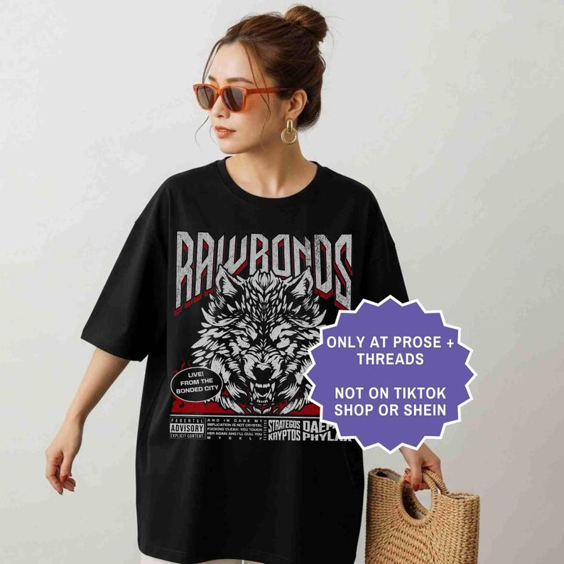Op de afbeelding: Zwart T-shirt met een wolfafbeelding en de tekst "RAWRANDS". Het shirt heeft ook de tekst "LIVE! FROM THE BONDED CITY" en "ONLY AT PROSE + THREADS NOT ON TIKTOK SHOP OR SHEIN".