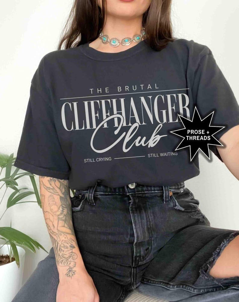 May include: Black t-shirt with white text that reads "The Brutal Cliffhanger Club" with the words "Still Crying" and "Still Waiting" below. A black star with white text that reads "Prose + Threads" is in the upper right corner.