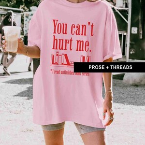 May include: Pink oversized t-shirt with the text "You can't hurt me." and a graphic of a bookshelf with books. The text below the graphic says "*I read unfinished book series".