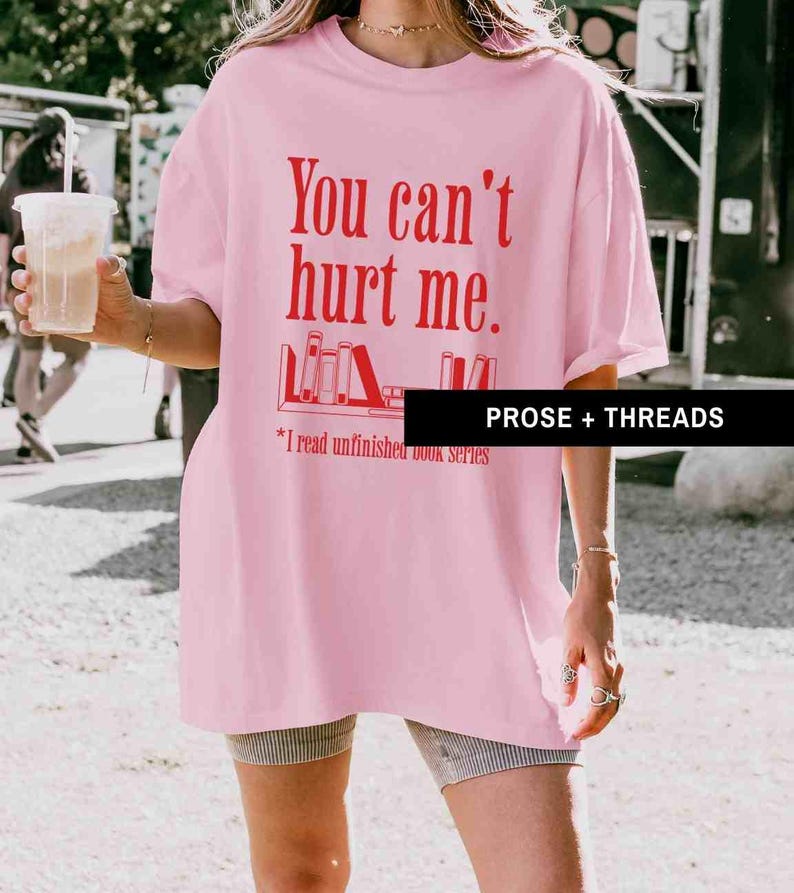 May include: Pink oversized t-shirt with the text "You can't hurt me." and a graphic of a bookshelf with books. The text below the graphic says "*I read unfinished book series".