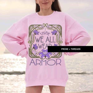 May include: A pink sweatshirt with a floral design and the text "I think we all wear armor".
