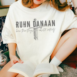 May include: A white t-shirt with a grey graphic of a sword and the text "Ruhn Danaan knew three things with absolute certainty".