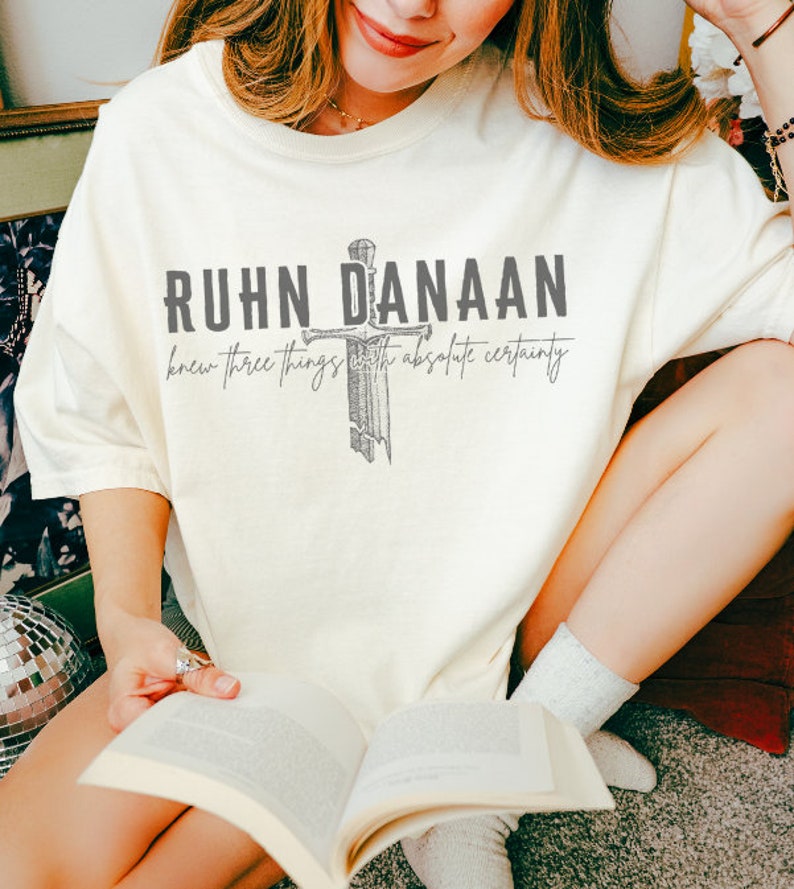 May include: A white t-shirt with a grey graphic of a sword and the text "Ruhn Danaan knew three things with absolute certainty".