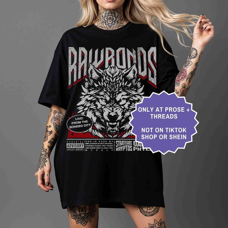 Op de afbeelding: Zwart T-shirt met een gedetailleerde wit en grijze wolf grafische afbeelding en de tekst "RAWRONDS". Extra tekst bevat "LIVE! FROM THE BONDED CITY" en "ONLY AT PROSE + THREADS".