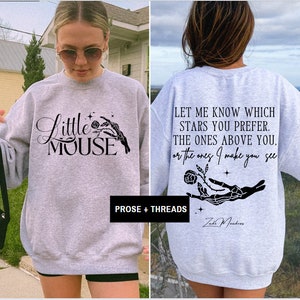 May include: A light gray sweatshirt with the text "Little Mouse" and a skeleton hand holding a rose on the front. The back of the sweatshirt has the quote "Let me know which stars you prefer..." and the name "Zad Meadows".