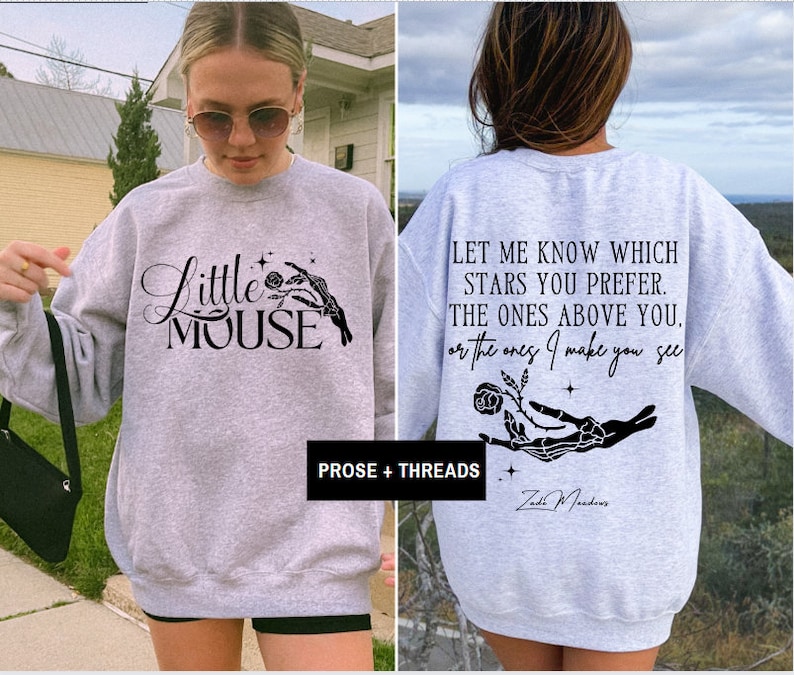 May include: A light gray sweatshirt with the text "Little Mouse" and a skeleton hand holding a rose on the front. The back of the sweatshirt has the quote "Let me know which stars you prefer..." and the name "Zad Meadows".