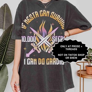 May include: Dark gray t-shirt with the text "IF NESTA CAN SURVIVE 10,000 STEPS I CAN DO CARDIO" in a circular design. The design includes crossed swords and flames in shades of purple, orange, and yellow.
