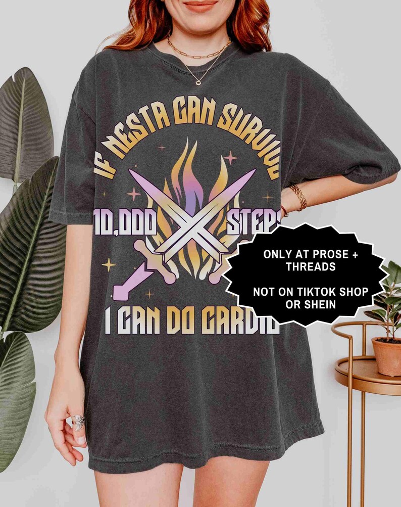May include: Dark gray t-shirt with the text "IF NESTA CAN SURVIVE 10,000 STEPS I CAN DO CARDIO" in a circular design. The design includes crossed swords and flames in shades of purple, orange, and yellow.