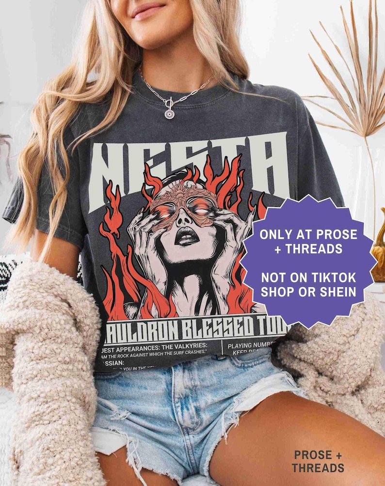 May include: Dark gray t-shirt featuring a graphic of a woman with flames and the text "MERTA". The shirt also has the text "AULORON BLESSED TOD". The shirt is from Prose + Threads and not on TikTok Shop or Shein.