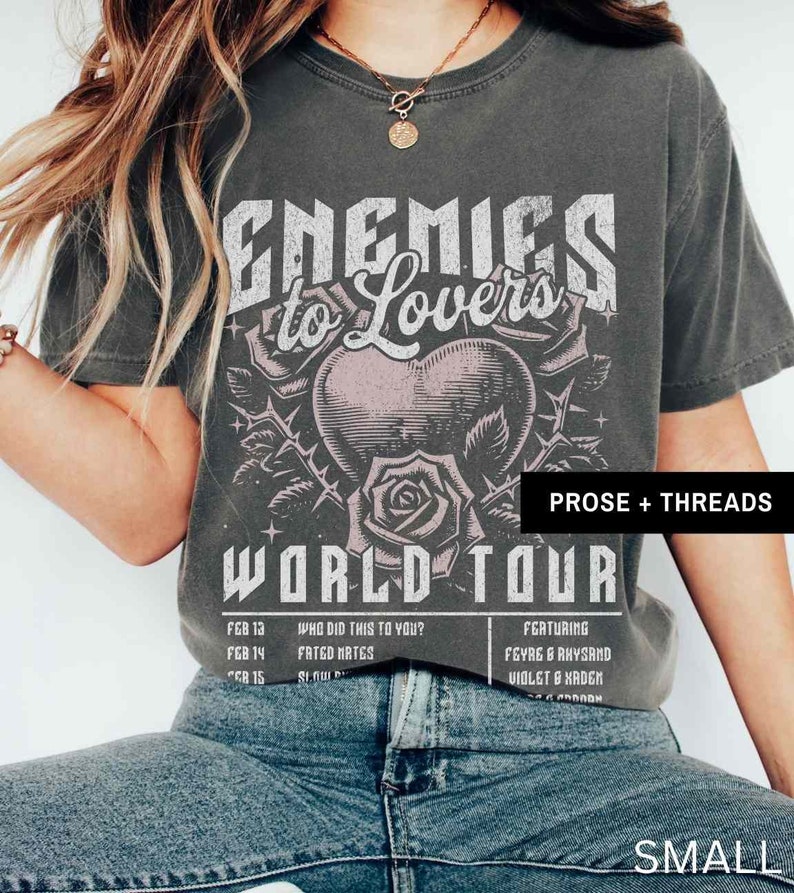 Pode incluir: Uma camiseta cinza com um design gr&aacute;fico de estilo vintage que apresenta um cora&ccedil;&atilde;o com espinhos, uma rosa e o texto "Enemies to Lovers World Tour". O texto "Prose + Threads" tamb&eacute;m est&aacute; inclu&iacute;do na camiseta. A camiseta &eacute; tamanho pequeno.
