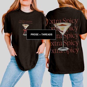 May include: Black t-shirt with a martini glass graphic and the text "I like my martinis like I like my books" on the front. The back of the shirt features a martini glass and the words "extra spicy" repeated. The brand name "PROSE + THREADS" is also visible.