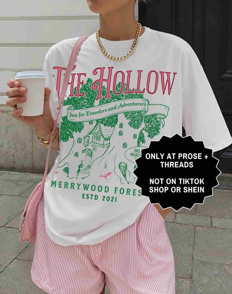 Pu&ograve; includere: T-shirt bianco con un design grafico con la scritta "THE HOLLOW" in rosa e verde, insieme a "Inn for Travelers and Adventurers" e "MERRYWOOD FORES ESTD 2021". La maglietta &egrave; abbinata a pantaloncini a righe rosa e bianche.