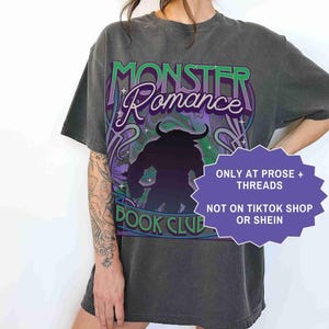Op de afbeelding: Een donkergrijs t-shirt met de woorden "MONSTER Romance BOOK CLUB" in groen en paars. Het shirt heeft een silhouet van een monster en de tekst "ONLY AT PROSE + THREADS NOT ON TIKTOK SHOP OR SHEIN". Het woord "PEPPER" staat onderaan.