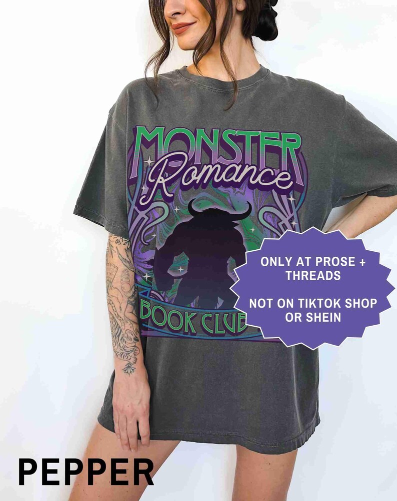 Op de afbeelding: Een donkergrijs t-shirt met de woorden "MONSTER Romance BOOK CLUB" in groen en paars. Het shirt heeft een silhouet van een monster en de tekst "ONLY AT PROSE + THREADS NOT ON TIKTOK SHOP OR SHEIN". Het woord "PEPPER" staat onderaan.