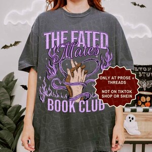 Pode incluir: Uma t-shirt cinzento-carv&atilde;o com um gr&aacute;fico de duas m&atilde;os entrela&ccedil;adas, rodeadas por chamas roxas e o texto "THE FATED Mates BOOK CLUB". Uma etiqueta vermelha em forma de estrela diz "ONLY AT PROSE + THREADS NOT ON TIKTOK SHOP OR SHEIN".