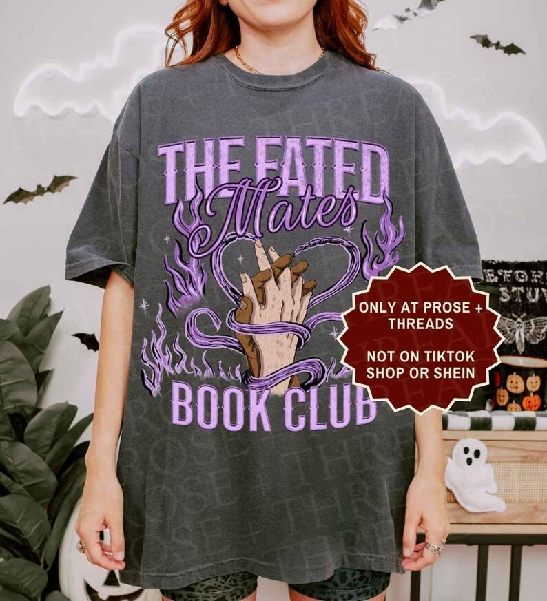 Pode incluir: Uma t-shirt cinzento-carv&atilde;o com um gr&aacute;fico de duas m&atilde;os entrela&ccedil;adas, rodeadas por chamas roxas e o texto "THE FATED Mates BOOK CLUB". Uma etiqueta vermelha em forma de estrela diz "ONLY AT PROSE + THREADS NOT ON TIKTOK SHOP OR SHEIN".