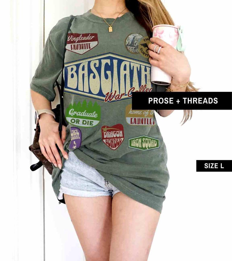 May include: Green oversized t-shirt with a vintage-style graphic print of "BASGIATH War College" and various patches, including "Vingleader Favorite", "Graduate or Die", "Dragon Bonder", "Iron Squad", and "Home of the Cauntile".