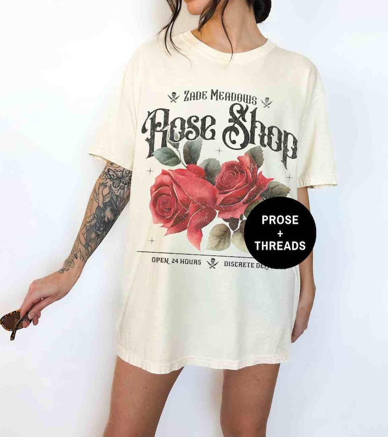 May include: A white oversized t-shirt with a vintage graphic design featuring a skull and crossbones, the text "Zade Meadows Rose Shop", two red roses, and the text "Open 24 Hours Discrete Delivery".