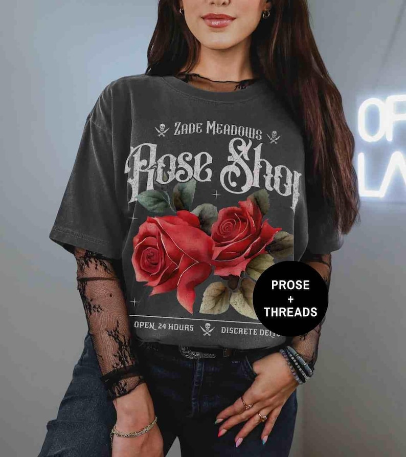 May include: Black t-shirt with a vintage-style graphic of red roses and the text "Zade Meadows Rose Shop" with skull and crossbones. The text "Open 24 Hours" and "Discrete Delivery" is also visible on the shirt.