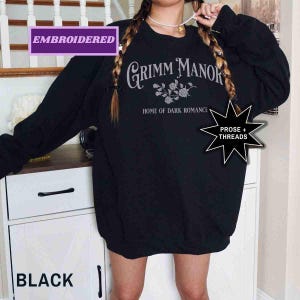 May include: Black embroidered sweatshirt featuring the text "Grimm Manor, Home of Dark Romance" in a gothic font. The sweatshirt also has a floral design and the words "Prose + Threads" in a starburst.