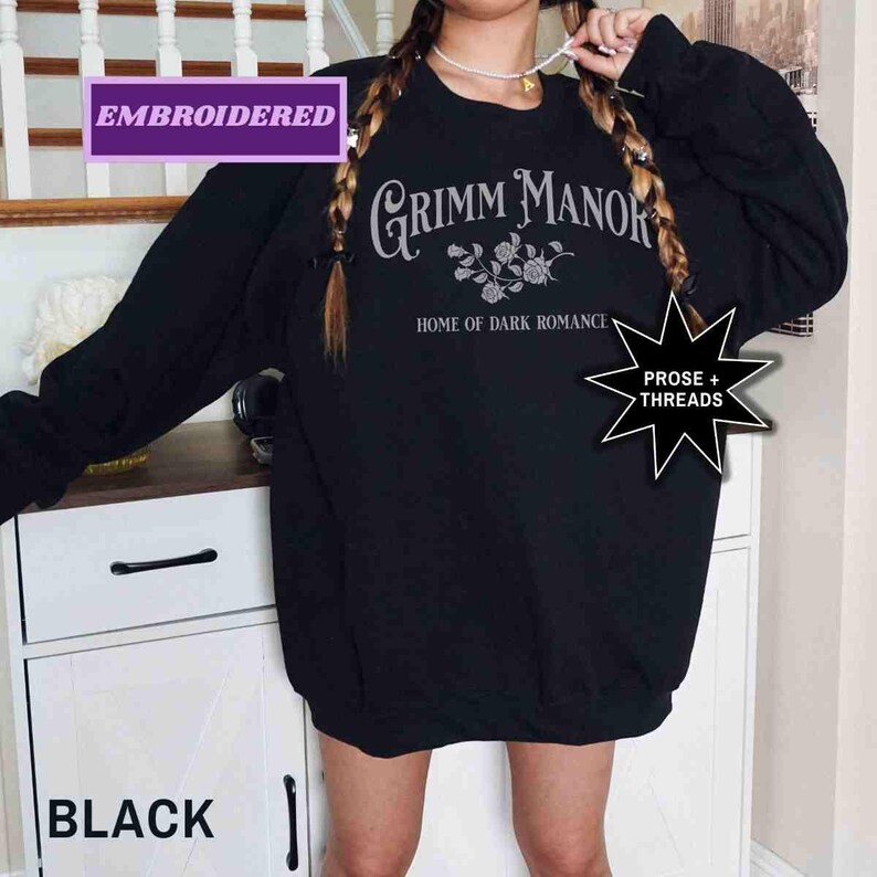 May include: Black embroidered sweatshirt featuring the text "Grimm Manor, Home of Dark Romance" in a gothic font. The sweatshirt also has a floral design and the words "Prose + Threads" in a starburst.