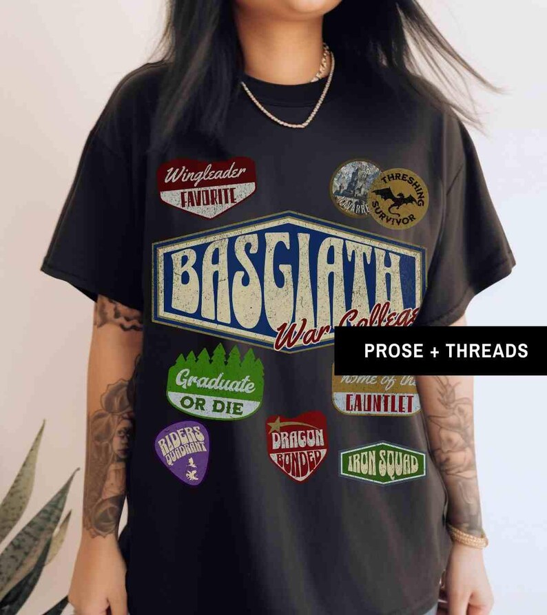 May include: Black t-shirt with a vintage-style graphic design featuring the text "Basgaathi War College" and various patches, including "Wingleader Favorite", "Thresing Survivor", "Graduate or Die", "Riders of the Radiant", "Dragon Bonded", "Home of the Gauntlet", and "Iron Squad".