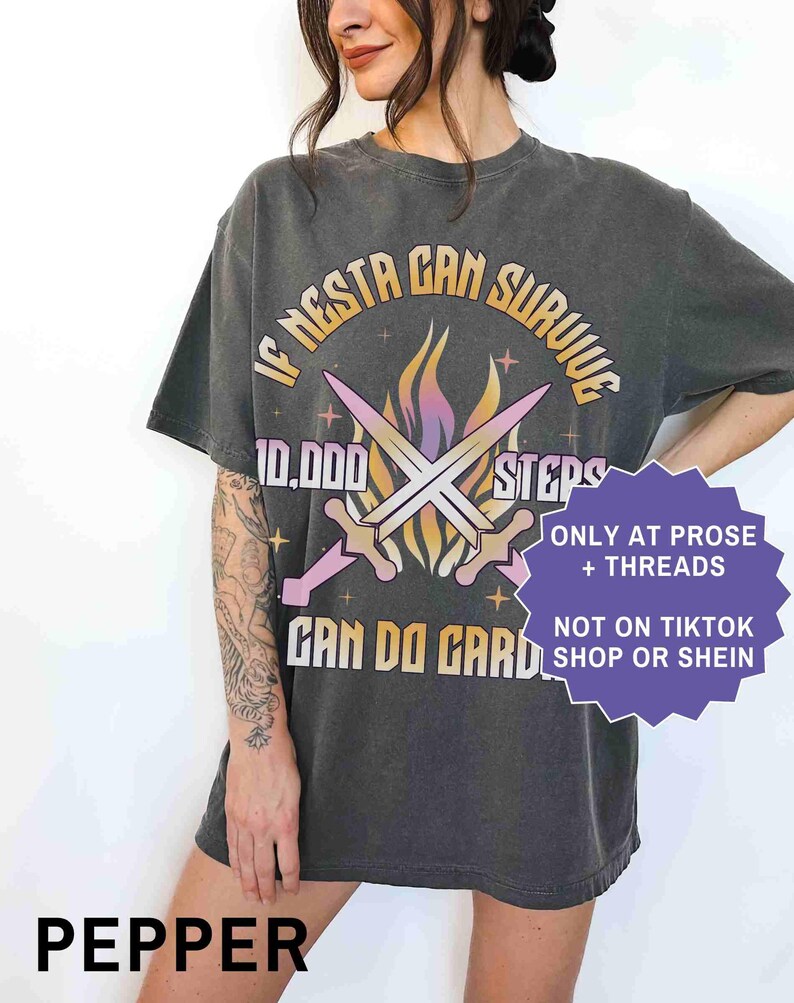 May include: Pepper-colored graphic tee with the text "IF NESTA CAN SURVIVE 10,000 STEPS CAN DO GARD." The design includes crossed swords and flames. Additional text reads "ONLY AT PROSE + THREADS" and "NOT ON TIKTOK SHOP OR SHEIN."