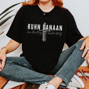 May include: Black t-shirt with a white graphic design featuring a sword and the text "RUHN DANAAN knew three things with absolute certainty."