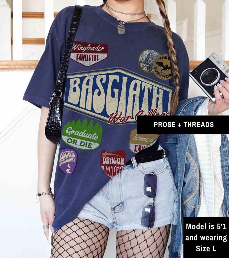 May include: A navy blue t-shirt with a vintage-style graphic design featuring the text "Basgaath War College" and various patches, including "Wingleader Favorite", "Graduate or Die", "Dragon Bonded", and "Three Survivor".