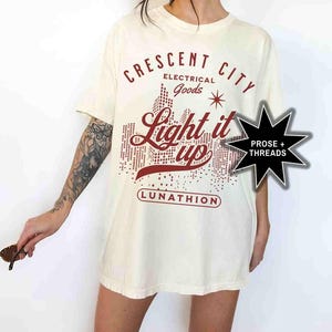May include: A white t-shirt with a red graphic design that says "Crescent City Electrical Goods Light it Up Lunathion".