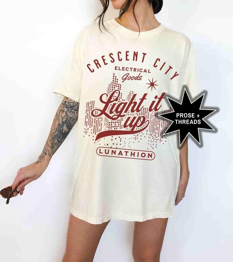 May include: A white t-shirt with a red graphic design that says "Crescent City Electrical Goods Light it Up Lunathion".