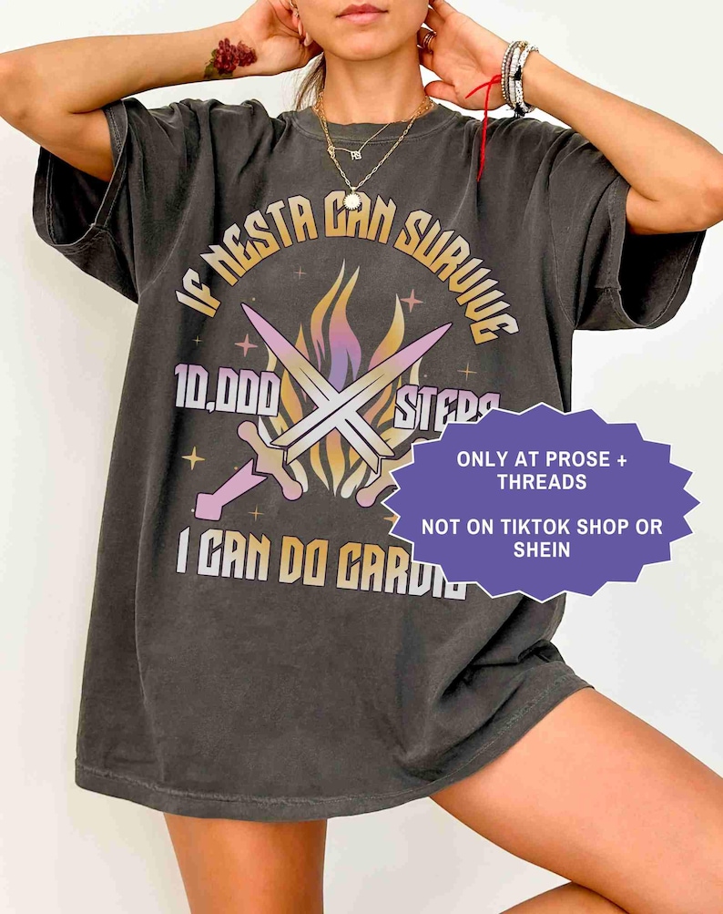 May include: Dark gray t-shirt with the text "IF NESTA CAN SURVIVE 10,000 STEPS I CAN DO GARDEN" in a gradient font. The design includes crossed swords and flames. The shirt also has the text "ONLY AT PROSE + THREADS NOT ON TIKTOK SHOP OR SHEIN".