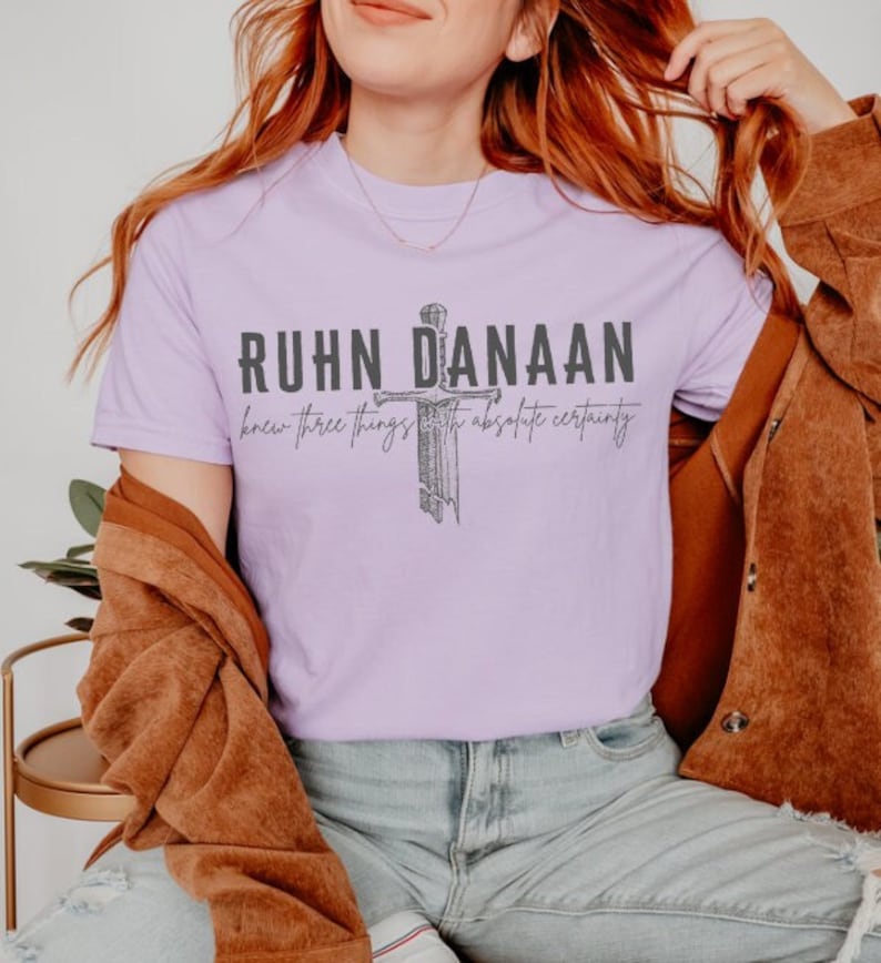 May include: A lavender t-shirt featuring a graphic of a sword and the text "Ruhn Danaan knew three things with absolute certainty".