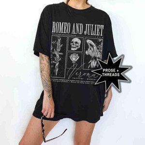 May include: Black t-shirt featuring a graphic design from Shakespeare's "Romeo and Juliet." The design includes a dagger, skull, rose, and angel wings. The word "Verona" is also featured. The shirt also has the text "PROSE + THREADS."