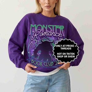 May include: A purple sweatshirt with the words "MONSTER Romance" in green and white script. Below the text is a silhouette of a monster. The words "BOOK CLUB '23" are at the bottom. A white and black sticker says "ONLY AT PROSE + THREADS NOT ON TIKTOK SHOP OR SHEIN".